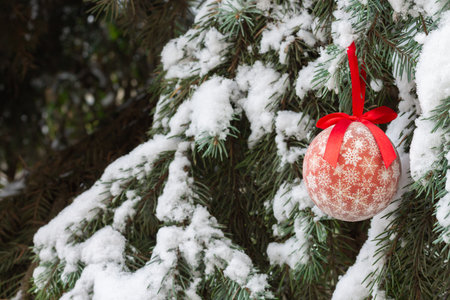 One red Christmas ball with ribbon hanging on snow Xmas tree outdoorsの写真素材