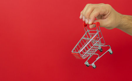 Man holding small shopping cart trolley over red background. Online shopping and fast delivery conceptの写真素材