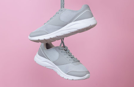 Female sport gray sneakers for run or fitness hanging on pink background closeup