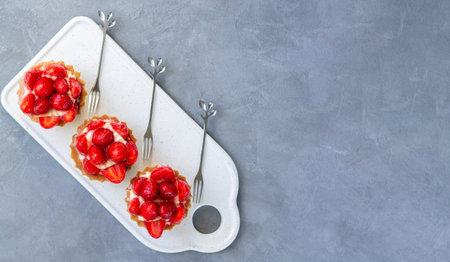 Three delicious strawberry tartlets with cream cheese on ceramic board top view. Copy space