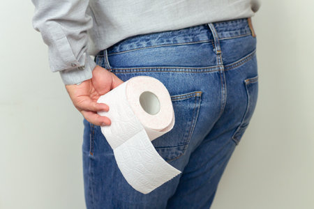 Man feeling pain and holding toilet paper roll close-up. Diarrhea, hemorrhoids or constipation conceptの写真素材