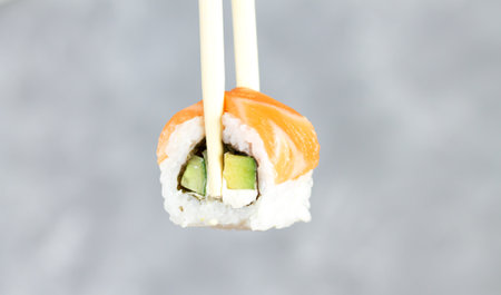 Eating sushi Philadelphia roll with chopsticks close-up. Japanese food sushi roll in restaurant.の写真素材