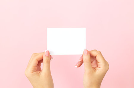 Female hands holding blank white business card, discount or flyer on pink background with copy space. Template for your designの写真素材