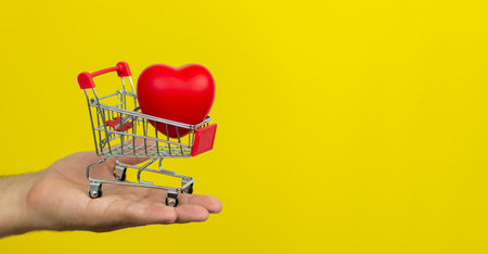 Man holding small cart with red heart on yellow background. Banner with copy spaceの写真素材