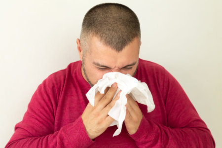 Young man holding handkerchief and sneezing on white background