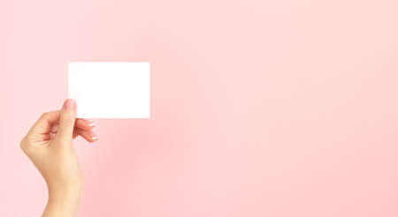 Woman hand holding blank white business card, discount or flyer on pink background with copy space. Template for your designの写真素材