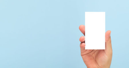 Person holding blank business card on light blue background. Banner with copy space