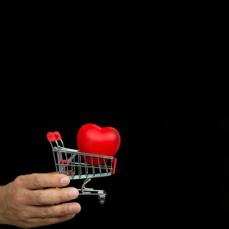 Hand with small shopping trolley and red heart on dark background