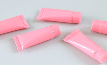 Five pink cosmetic tubes on gray background close-up. Spa product containers design