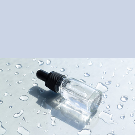 Cosmetic skincare serum in transparent glass bottle on gray background with water drops
