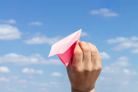 Origami paper plane in young male hand on blue cloudy sky backgroundの写真素材