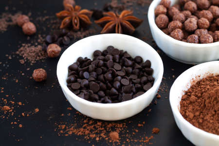 Chocolate morsels and cocoa powder in bowls on dark slate table, dessert cooking ingredients backgroundの写真素材