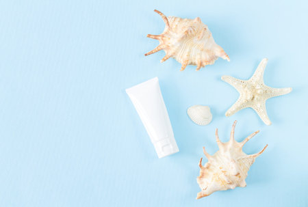 Blank unbranded white plastic cosmetic tube next to sea shells top view on light blue summer...