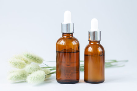 Two glass brown dropper bottles mockup next to dried flowers. Set of luxury organic cosmetic...