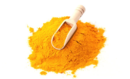 Pile of turmeric or curcuma powder with wooden scoop isolated on white background wih copy space....