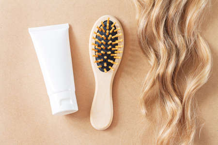 Lock of wavy blonde hair, comb brush and tube of hair care product top viewの写真素材