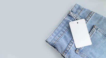 Blank white cardboard tag or label with rope on jeans clothes backgroundの写真素材