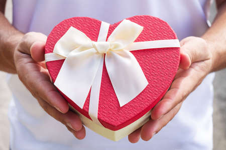 Man holding beautiful red heart shape gift box with ribbon bow close-upの写真素材
