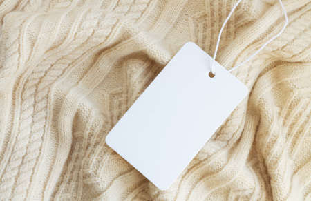 Mock-up of blank white paper price tag or label on warm sweater background close-upの写真素材