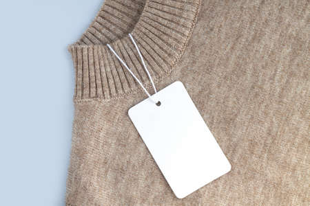 Mock-up of blank white paper price tag or label on warm sweater background close-upの写真素材
