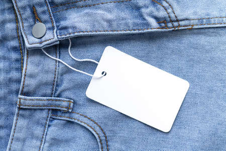 Blank white cardboard tag or label with rope on jeans clothes backgroundの写真素材