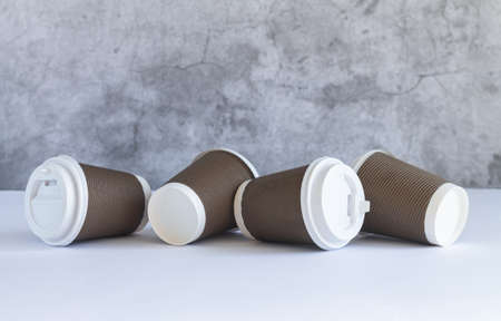 Four brown disposable paper coffee cup with white caps on wooden table. Takeaway drink and eco-friendly tableware conceptの写真素材