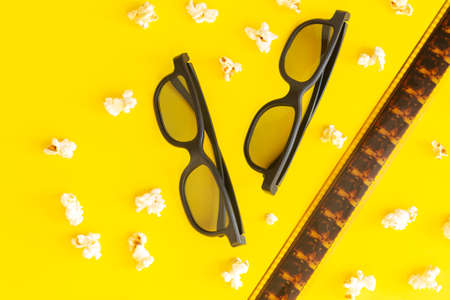Movie time concept, cinema background with popcorn, 3d glasses and filmstrip top view on yellow tableの写真素材