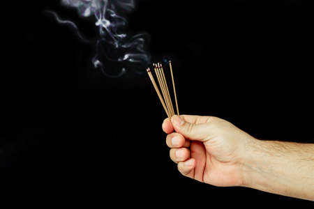Male hand holding set of smoldering incense sticks with aroma smoke on dark backgroundの写真素材