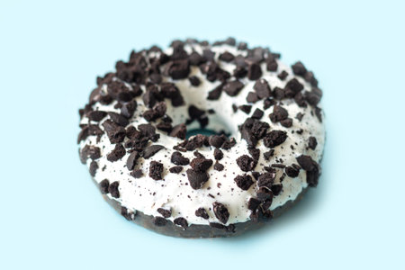 Tasty white chocolate glazed donut with dark cookies crumbs on light blue background