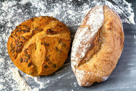 Bakery background with two different freshly baked crispy bread on flour kitchen table