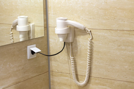 White hair dryer on beige ceramic wall tiles in hotel bathroom. Hotel accommodation service conceptの写真素材