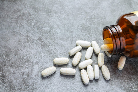 White medical pills spilling out of open drug bottleの写真素材