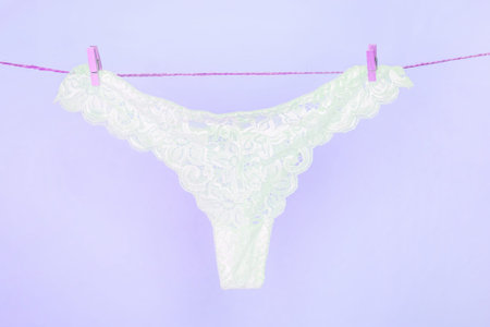 Female white sexy lace panties hanging on clothesline on light purple backgroundの写真素材