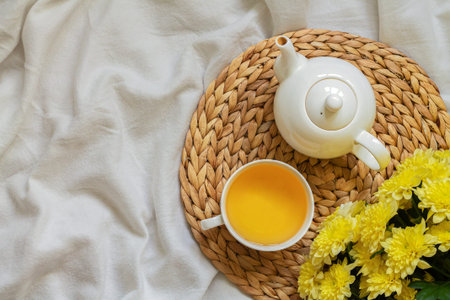 Herbal tea with white tea cup and teapot on rattan tray standing on bed. Tea concept, top viewの写真素材