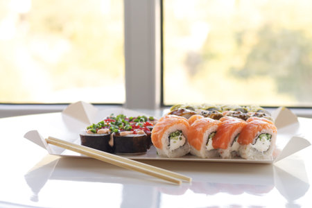 Tasty sushi rolls in disposable paper box on white table. Delivery service Japan food in eco...