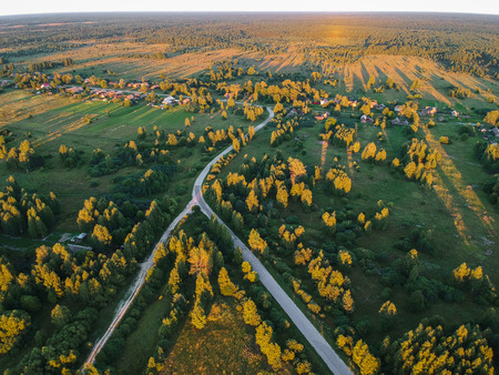 The road among the forest to the village at sunset from a heightの写真素材