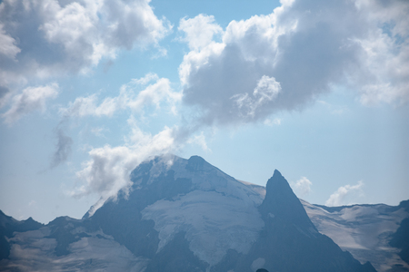 The peaks of the Caucasus Mountains in cloudy clouds and the rays of the sun through them in the outskirts of Dombai. And on the tops of snow lies.の写真素材