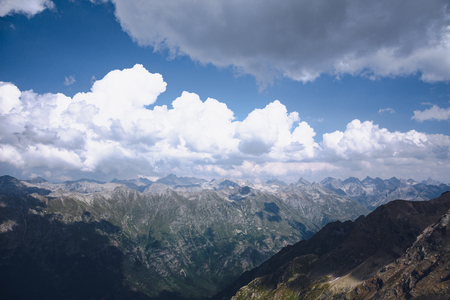 The peaks of the Caucasus Mountains in cloudy clouds and the rays of the sun through them in the outskirts of Dombai. And on the tops of snow lies.の写真素材