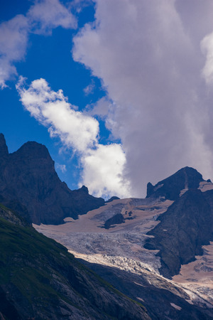 Massive peaks of the Caucasus Mountains in the snow in the surroundings of dombai in the clouds. Summer day.の写真素材