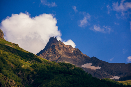 Massive peaks of the Caucasus Mountains in the snow in the surroundings of dombai in the clouds. Summer day.の写真素材