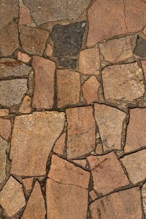 The texture of the sidewalk of chaotic granite stones of different colors with many cracks