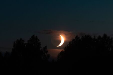 New moon the moon comes over the forest on a summer evening. The moon illuminates the clouds.の写真素材