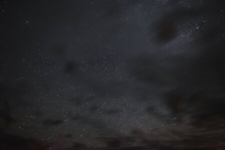Stars in the night sky through the clouds on a summer nightの写真素材