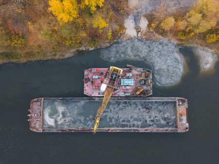 Aerial view: River crane shifts silt from barge in autumnの写真素材