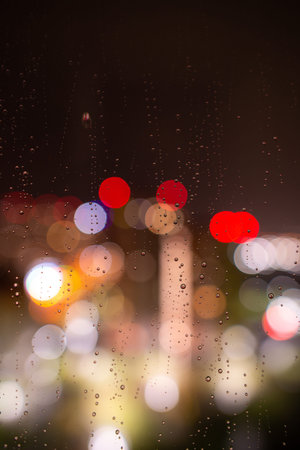 Raindrops on the window glass at night against the background of bokeh from the lights and Windows...