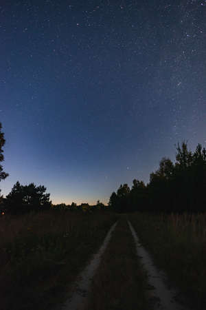A large panorama, a country road stretching away into the fields to the forest. Starry sky with the Milky Way overheadの写真素材