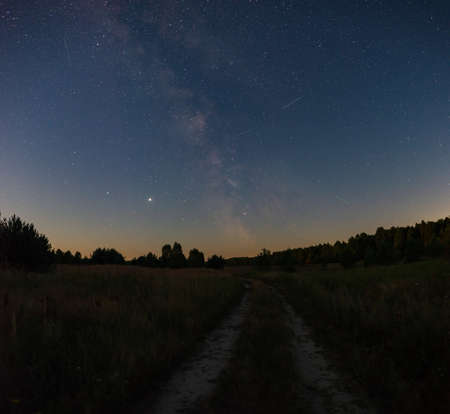 A large panorama, a country road stretching away into the fields to the forest. Starry sky with the Milky Way overheadの写真素材