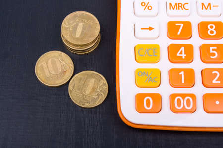 Calculator and coins lying on dark wooden surfaceの写真素材
