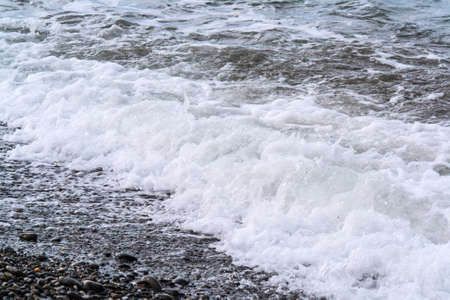 Turbulent sea waves roll on the shore of pebblesの写真素材