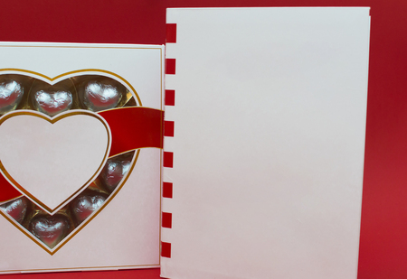 Beautiful love concept for Valentines day. Romantic box of sweets and modern note book on the red background.の写真素材